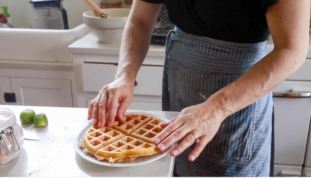 women wearing a blue stripped apron placing a cheddar waffle on a white plate on her white kitchen island