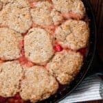 sourdough cherry cobbler in a cast iron skillet on top of a wood table with a blue and white stripped napkin