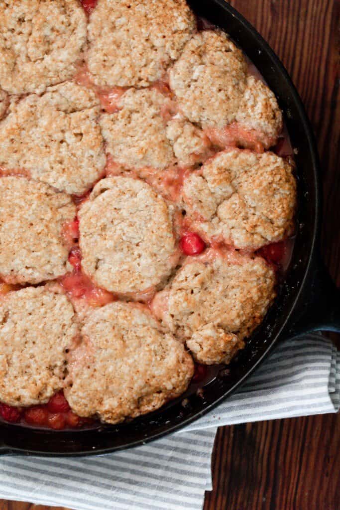 sourdough cherry cobbler in a cast iron skillet on top of a wood table with a blue and white stripped napkin