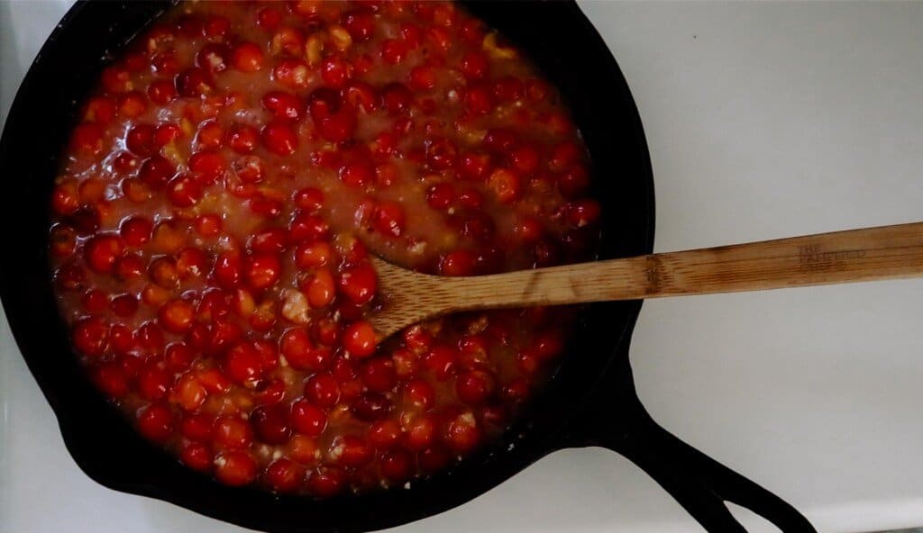 cherry filling in a cast iron skillet with a wooden spoon in the filling. The skillet sits on a white quartz countertop