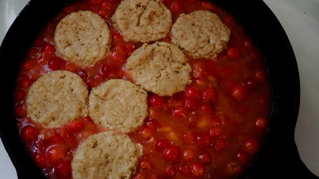 sourdough cobbler biscuit topping being placed on cherry filling in a cast iron skillet