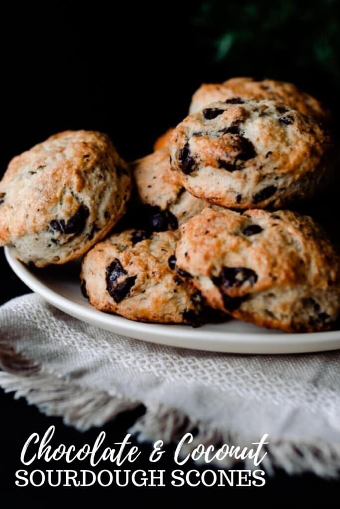 sourdough scones with chocolate chips and coconut stacked on a cream colored plate on a cream colored woven towel