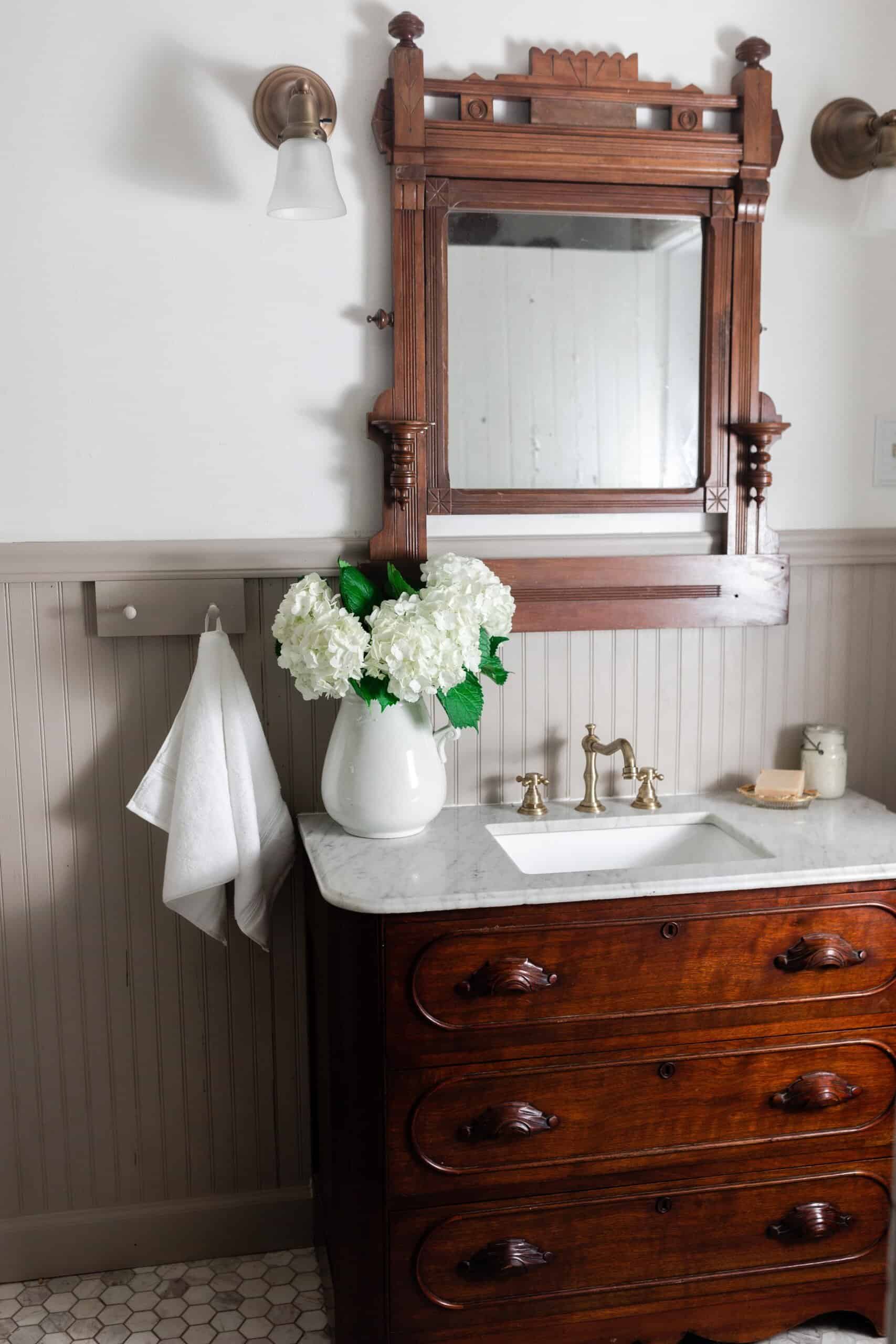 Antique dresser turned into a vanity with a marble tub with a ornate wood mirror. Bead board graces the walls and antique accessories