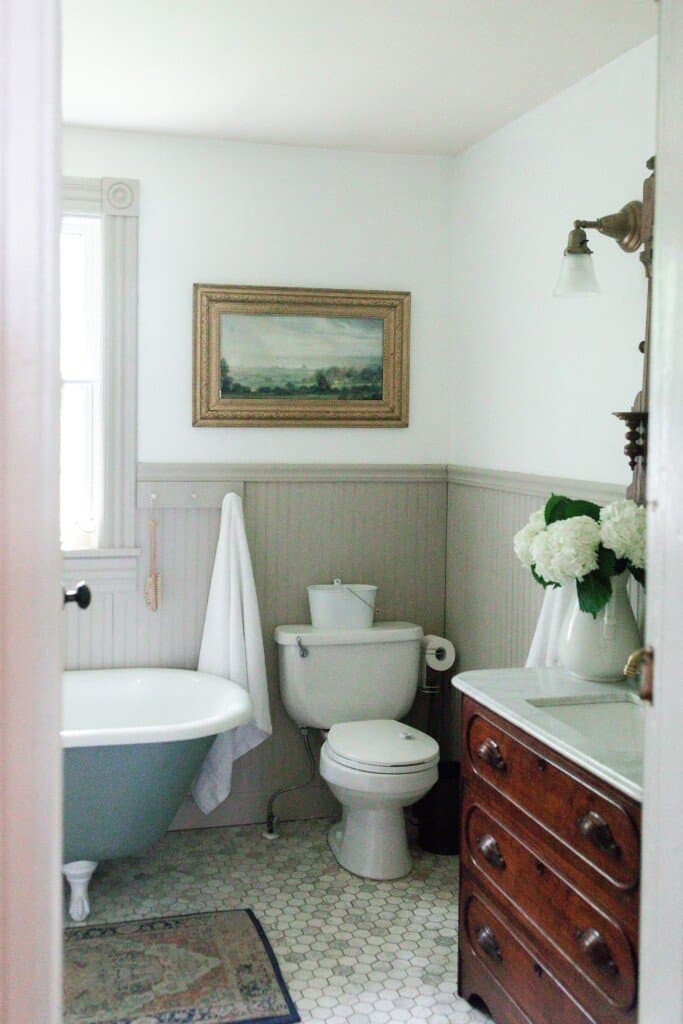 Farmhouse bathroom renovation with marble floors, a blue green clawfoot tub, and vintage dresser turned sink