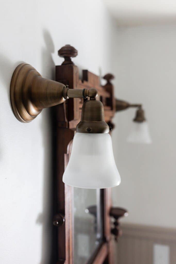 two brass sconce lights hanging on each side of a wooden antique mirror