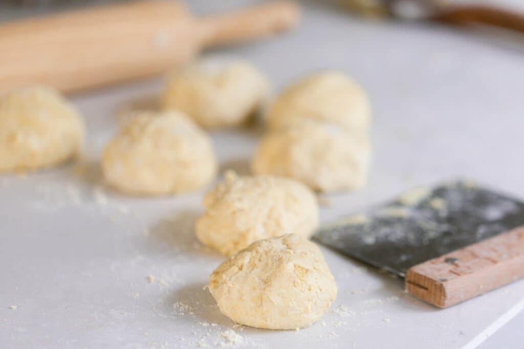 einkorn flat bread dough balls on a white countertop with a bench strapped to the right and a rolling pin behind the dough