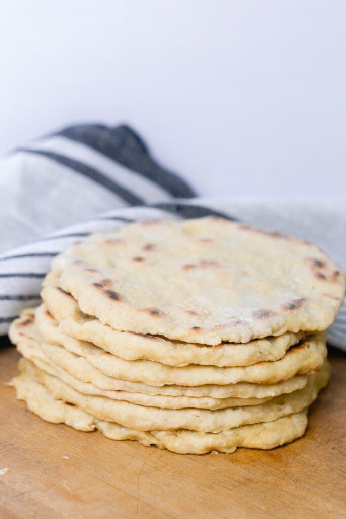 einkorn flat bread stacked on a wood cutting board 7 high with a black and gray stripped towel in the background