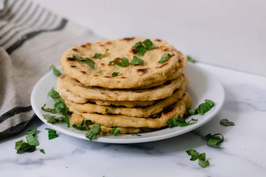 stack of einkorn flatbread with herbs on a white plate on a white and gray quartz countertop