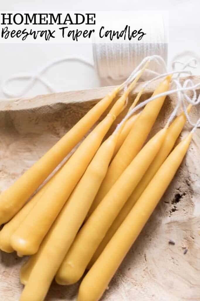 seven hand dipped tampered beeswax candles laying in a wooden bowl with a spool of wick behind the bowl