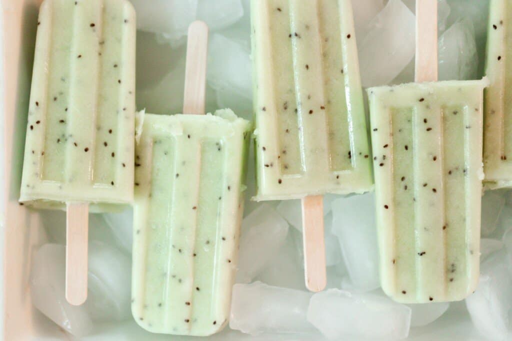 four green kiwi lime popsicles laying on a bed of ice