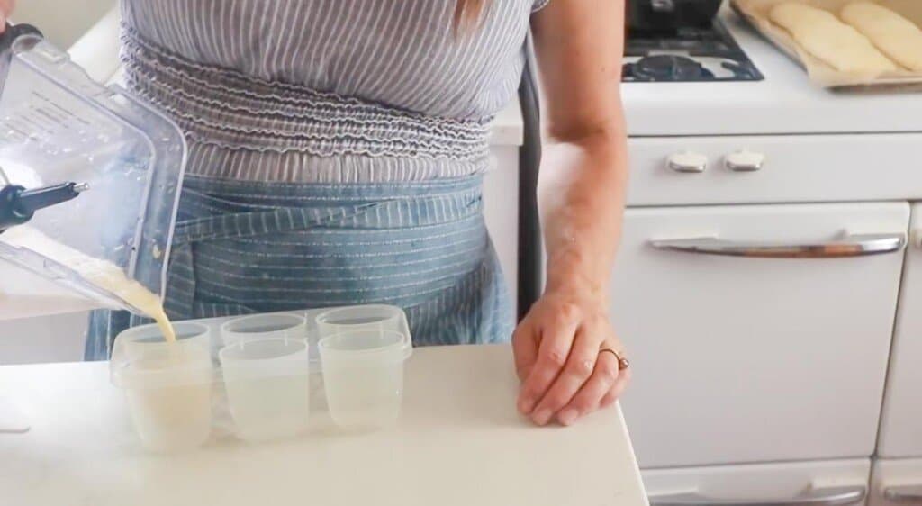 women wearing a blue apron pouring a blender full of milk, honey, and  orange juice into a popsicle mold.