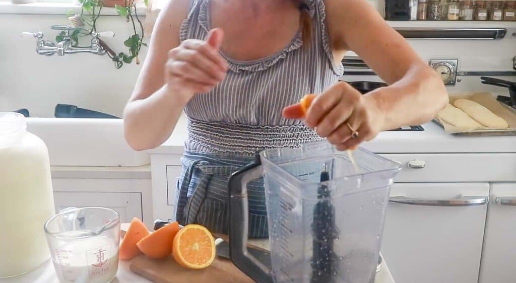 women wearing a blue apron squeezing and orange into a blender