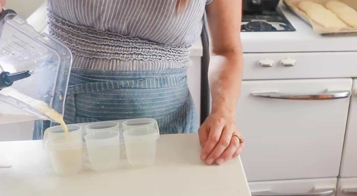 women wearing a blue apron pouring a blender full of milk, honey, and orange juice into a popsicle mold.