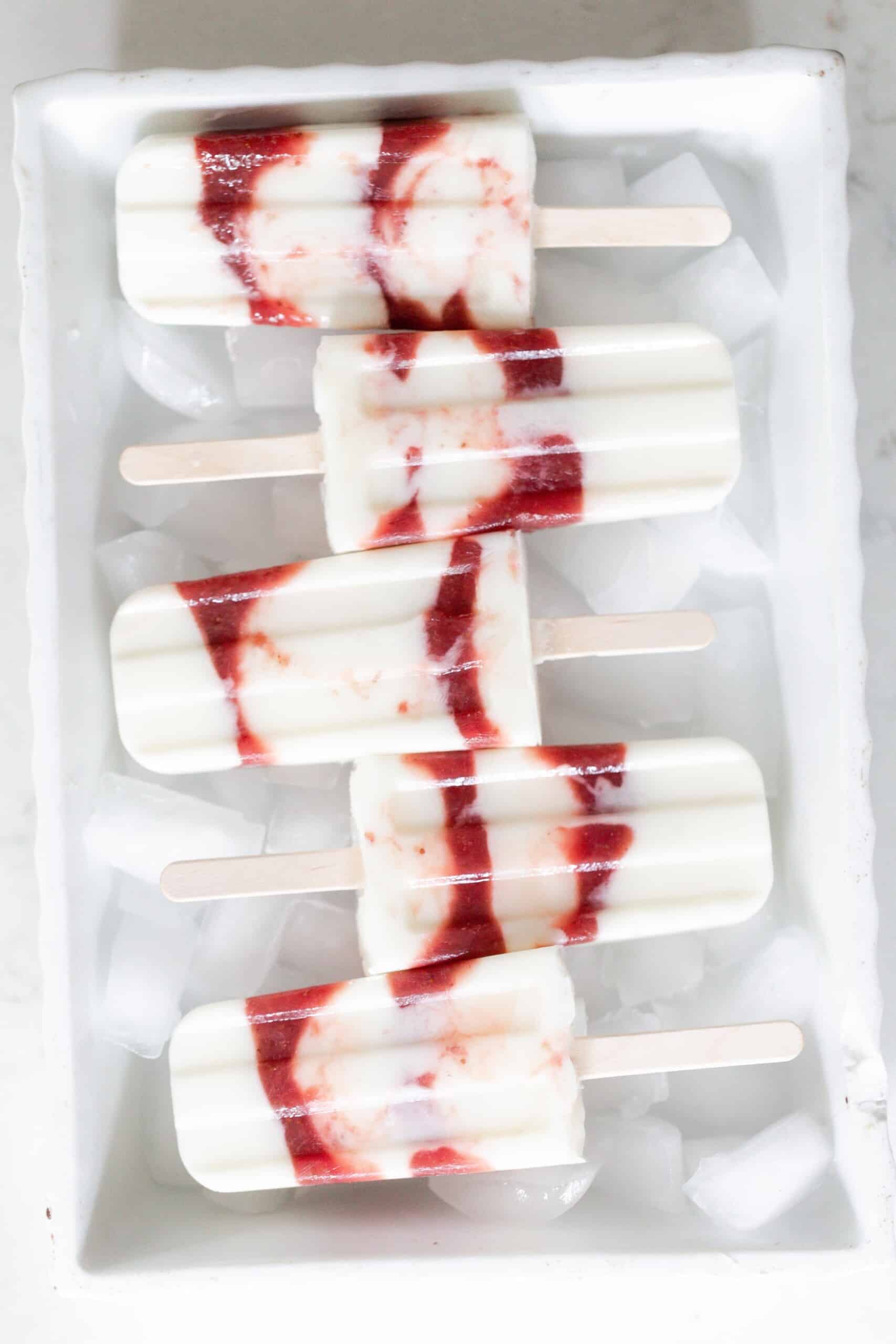 five strawberry yogurt popsicles laying on top of ice cubes in a white dish