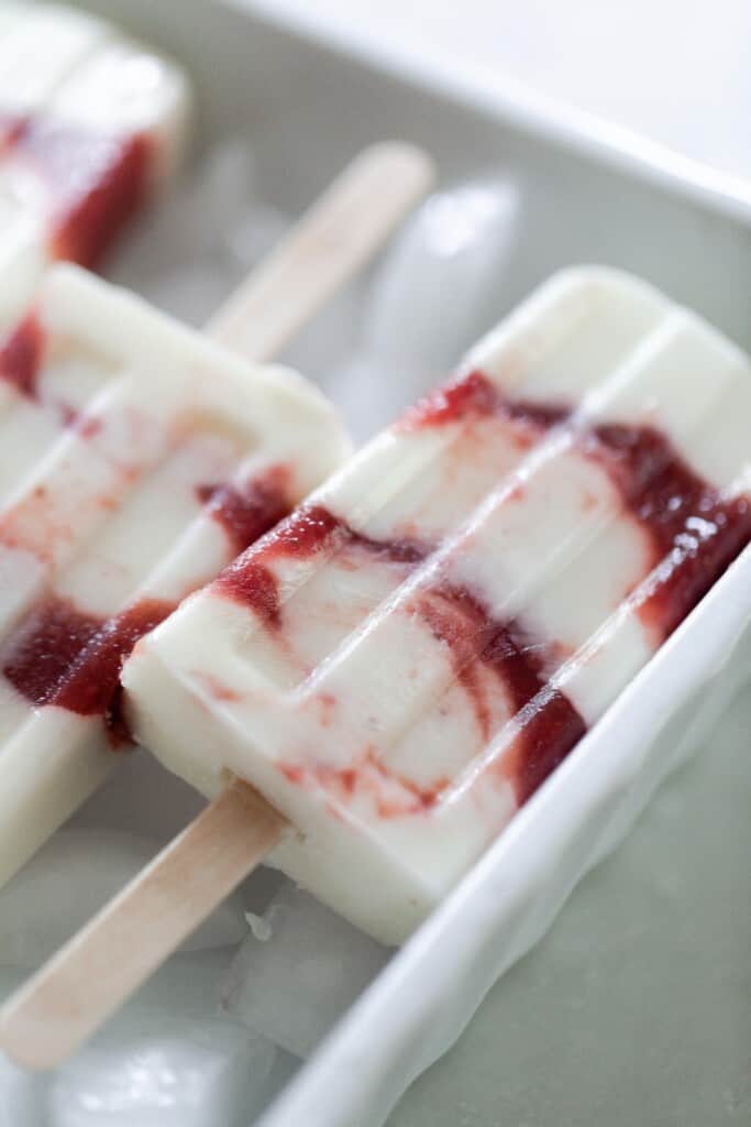close up picture of a strawberry yogurt popsicle on a bed of ice cubes.