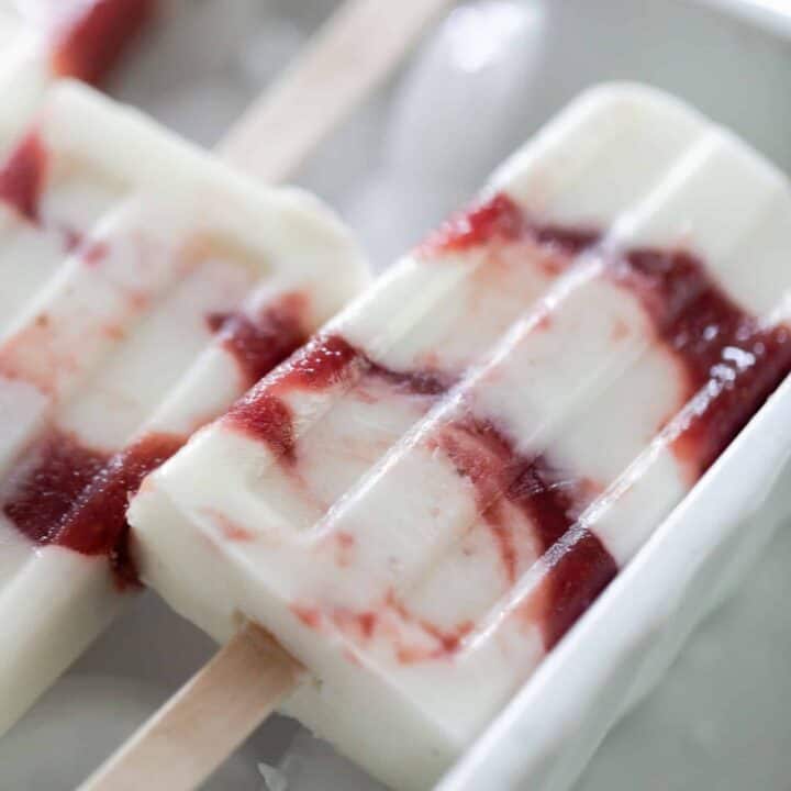 close up picture of a strawberry yogurt popsicle on a bed of ice cubes.