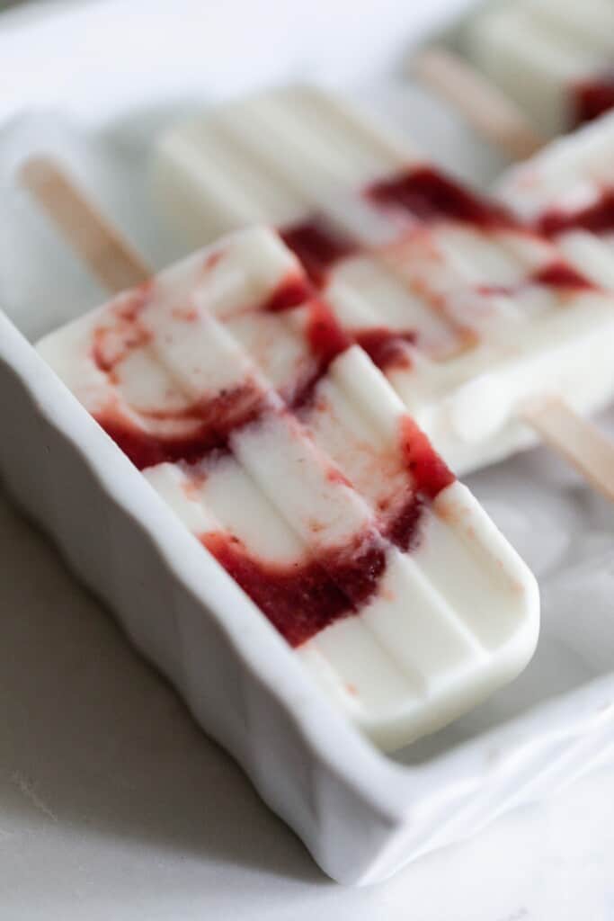 white and red stripped yogurt popsicles in a white dish with ice cubes