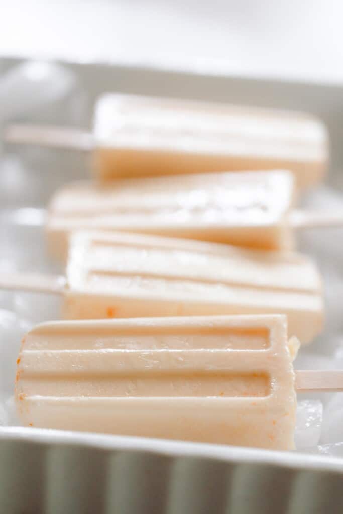 four creamy orange creamsicle popsicles in a white baking dish with ice