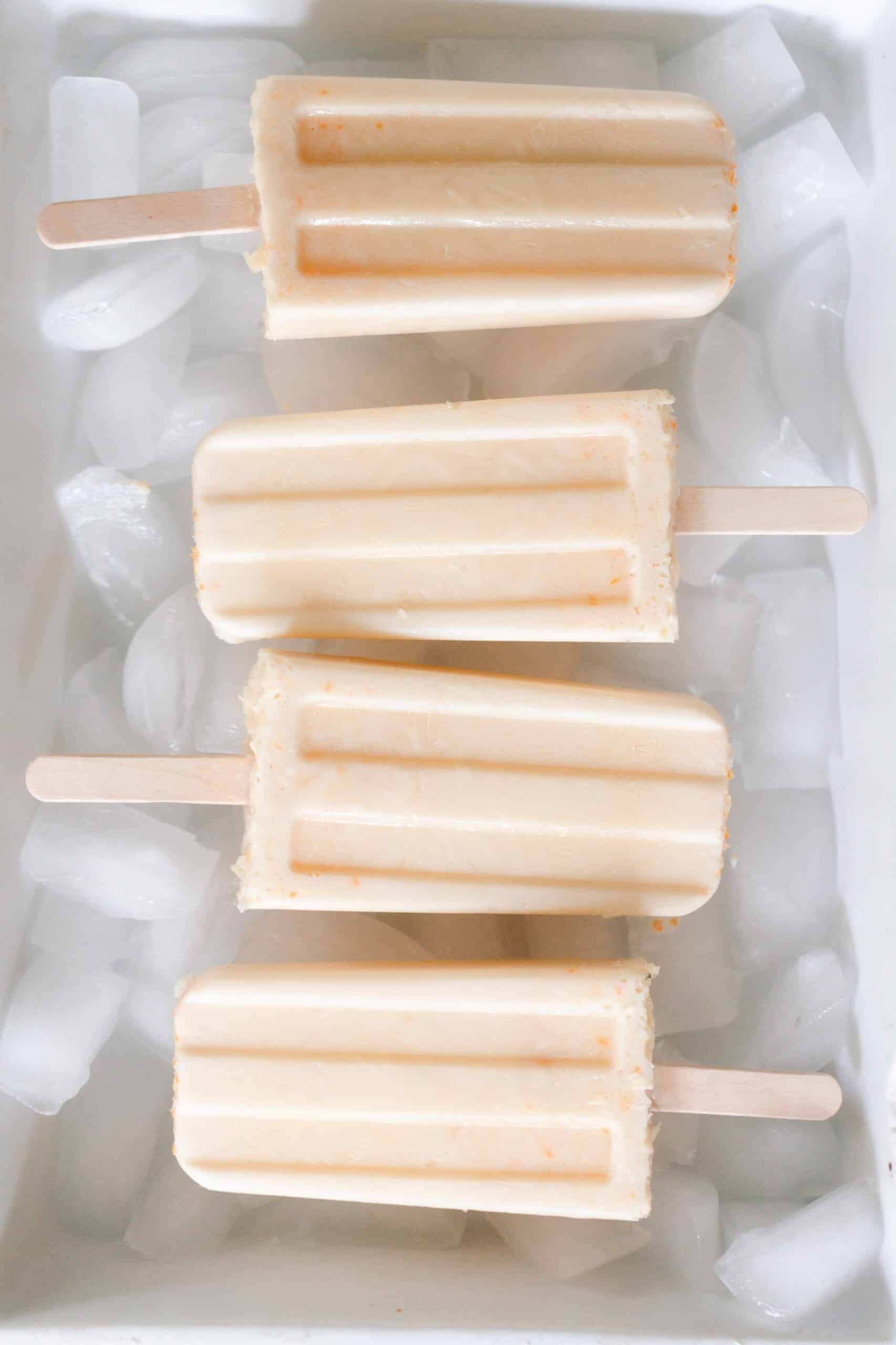 overhead photo of four orange creamsicle popsicles in a white dish full of ice
