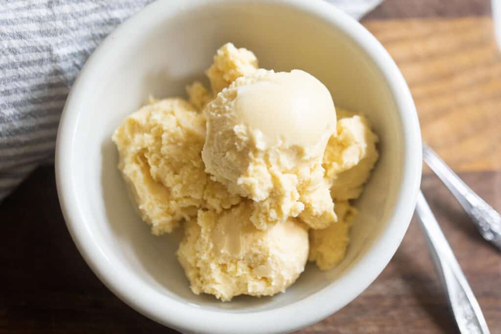 overhead photo of raw milk vanilla ice cream in a white bowl on a wood table with spoon to the right