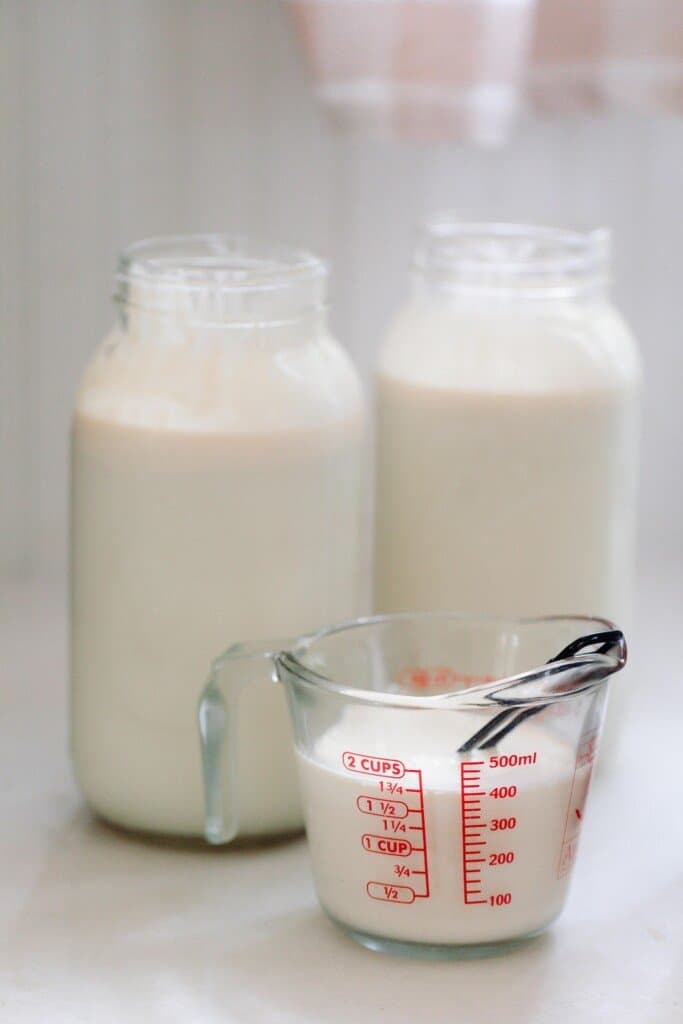 half gallon jars of raw milk with a glass measuring cup of milk in front of the jars
