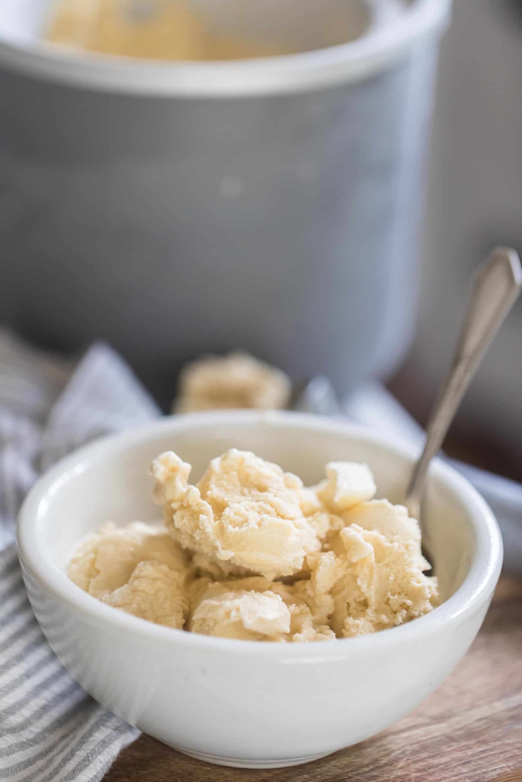 raw milk ice cream in a white bowl with a spoon on a wooden table with the ice cream canister in the background