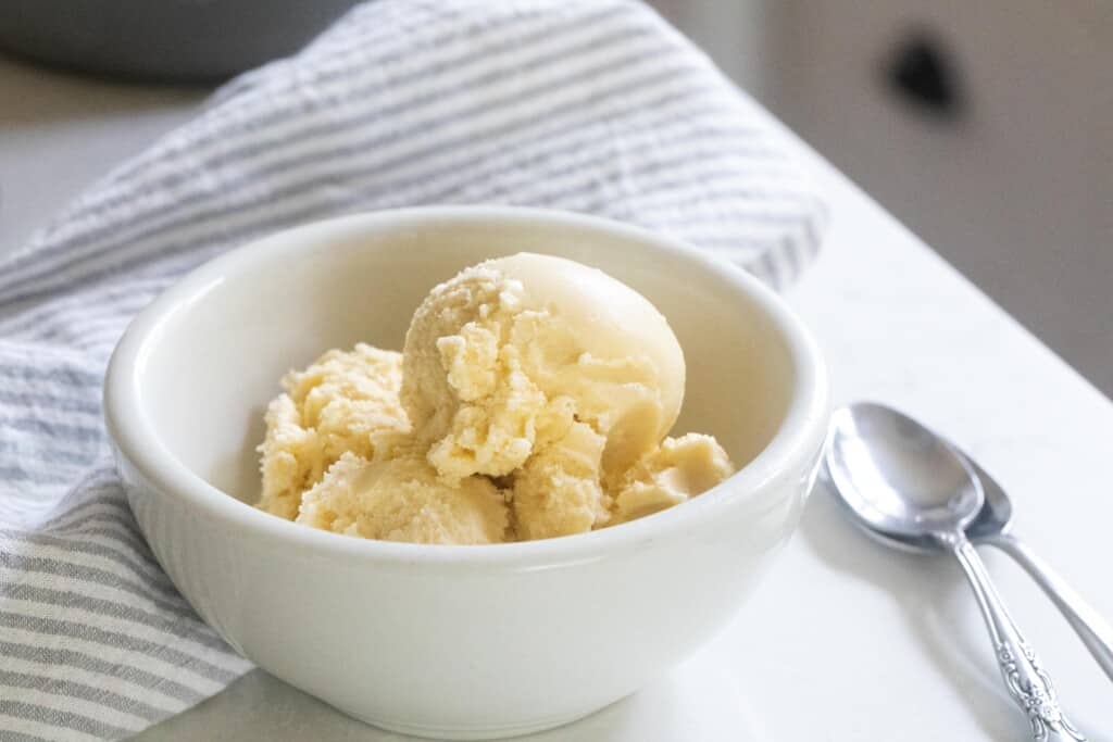 overhead photo of raw milk ice cream scooped into a white bowl on a white and gray stripped towel with a spoon to the right