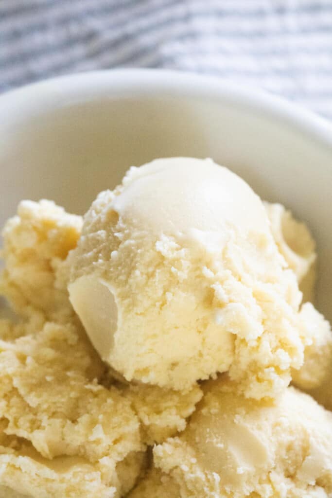 close up picture of raw milk ice cream scooped into a white bowl with a gray and white stripped towel inn the background