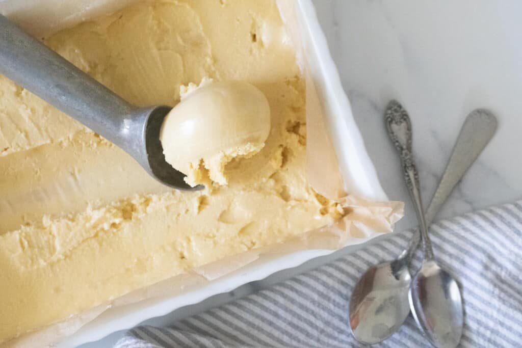 raw milk ice cream in a metal pan with a ice cream scoop scooping out the ice cream