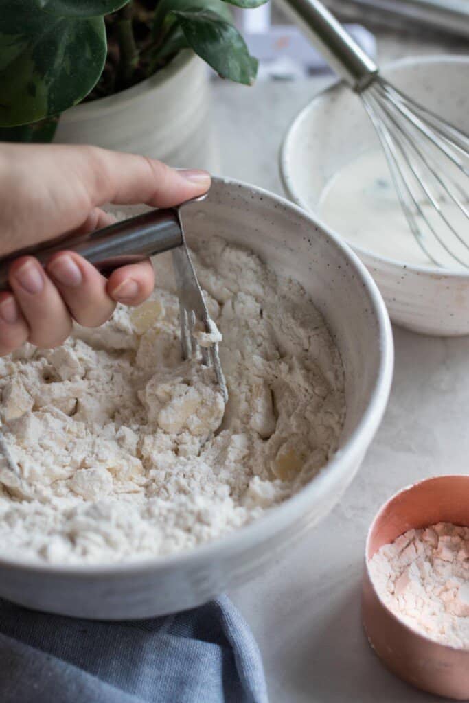 pastry blender cutting in butter into flour in a white bowl. Another bowl sits directly behind