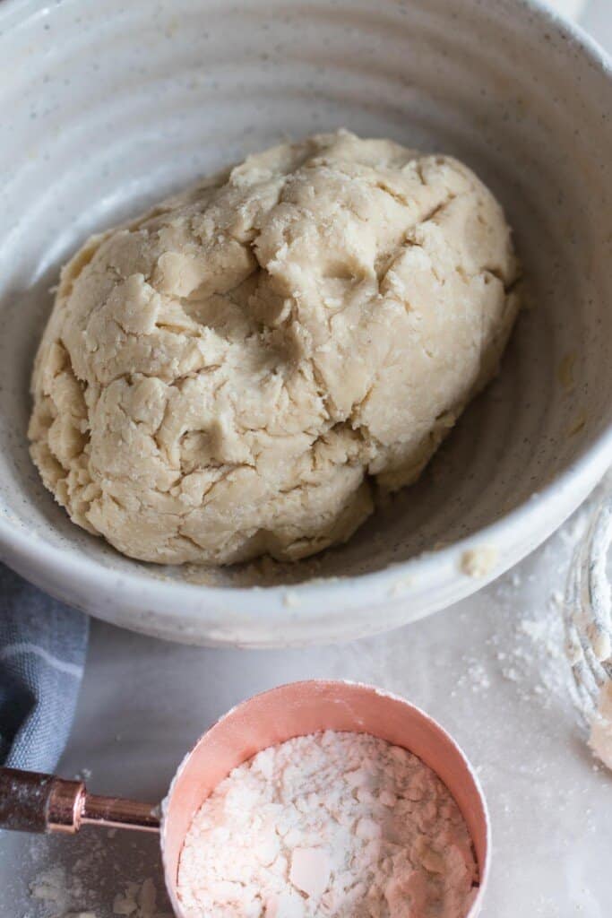 sourdough shortcake dough kneaded into a ball into a stone bowl. A cup of flour sits in front.