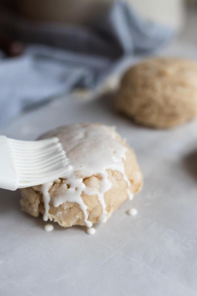 pastry brush brushing cream over a raw sourdough biscuits on a parchment lined cookie sheet before baking