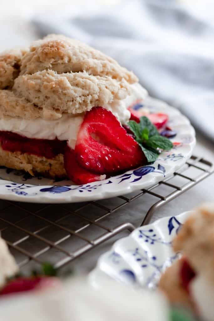 sourdough biscuits with strawberry sauce and homemade whipped cream sandwiched between the biscuits on a blue and white plate with extra strawberries to garnish