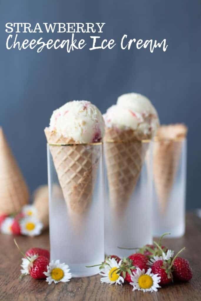 cones filled with strawberry cheesecake ice cream in cones in glasses on a wood table with strawberries and flowers spread across the table