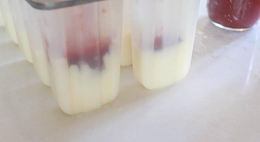 yogurt and strawberry jam being added to a popsicle mold in layers