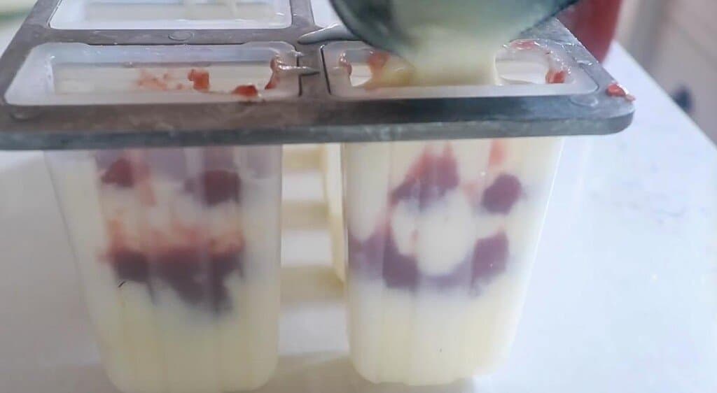 yogurt being poured into a popsicle mold with yogurt being poured on top.