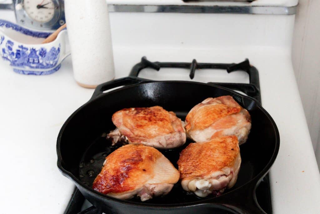 four chicken thighs browning in a fast iron skillet
