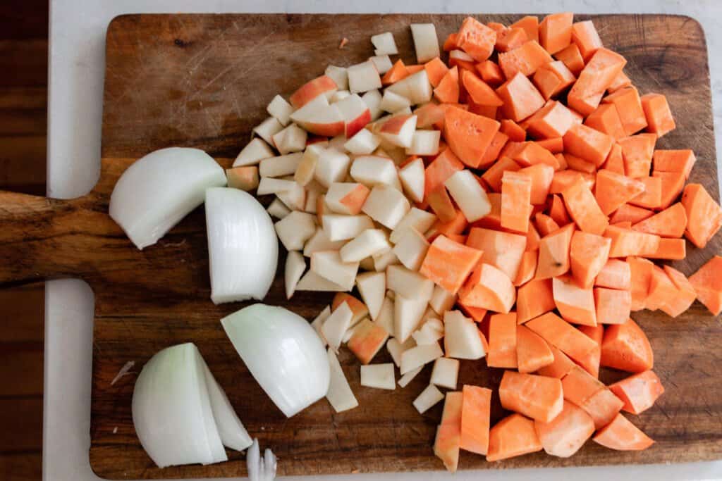apples, sweet potatoes, and onions diced on a wood cutting board