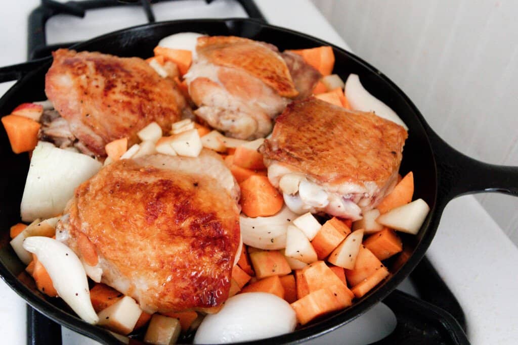 sweet potatoes, apples, and onions arranged around a four browned chicken thighs