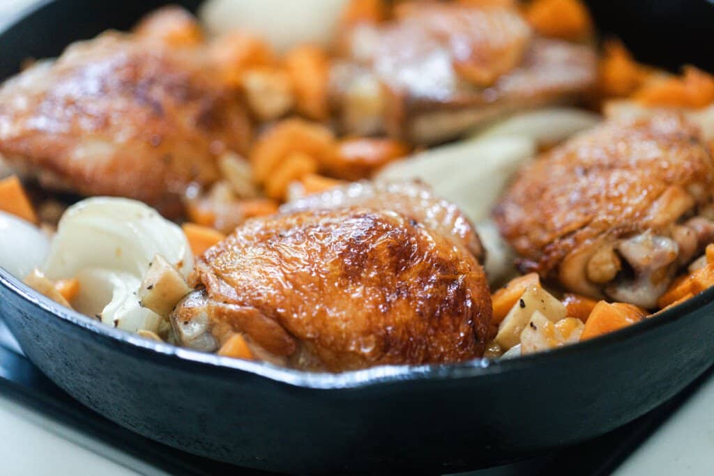 crispy chicken thighs with sweet potatoes, onions, and apples in a cast iron skillet and topped with thyme 
