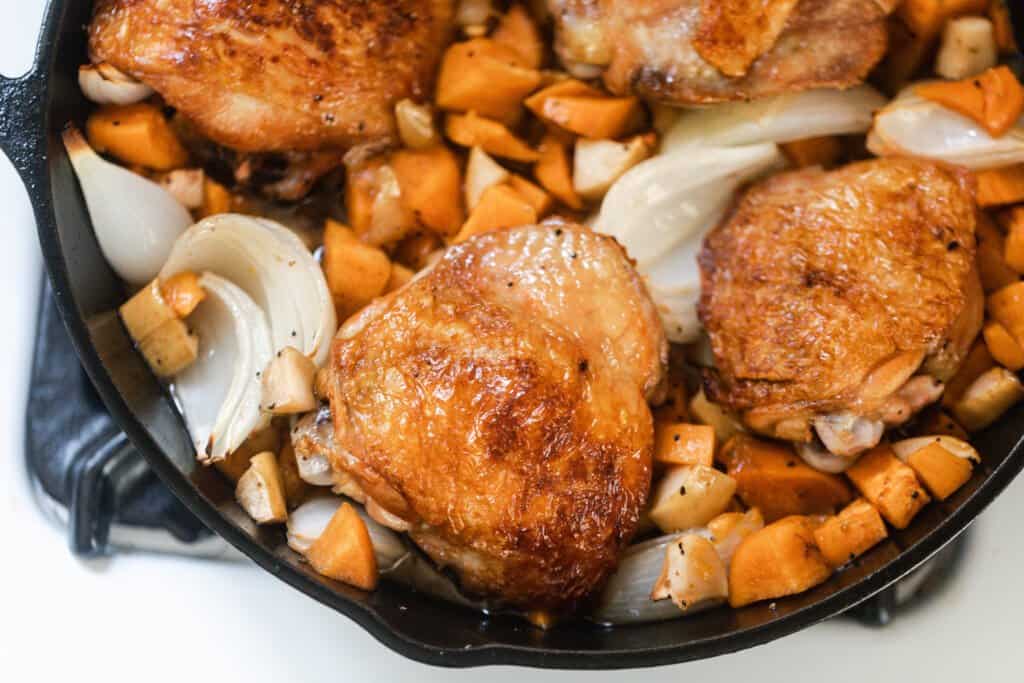 maple roasted chicken with sweet potatoes, onions, and apples in a cast iron skillet