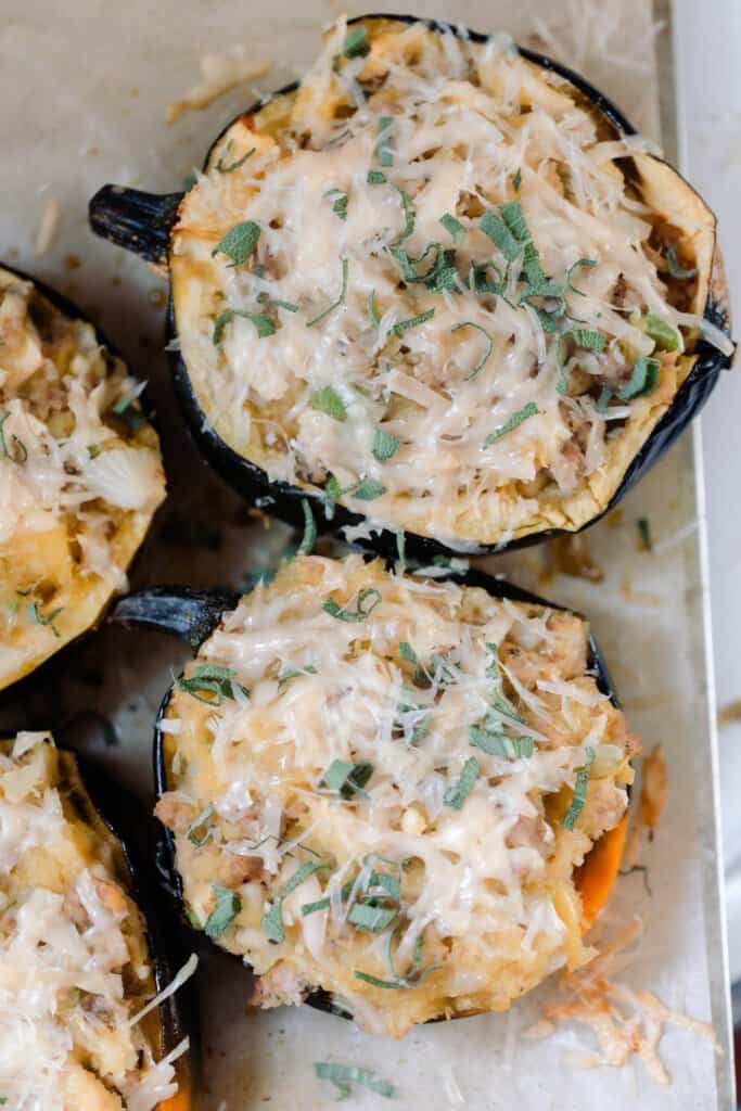 overhead photo of Sausage and Apple Stuffed Acorn Squash topped with parmesan and fresh sage on parchment paper