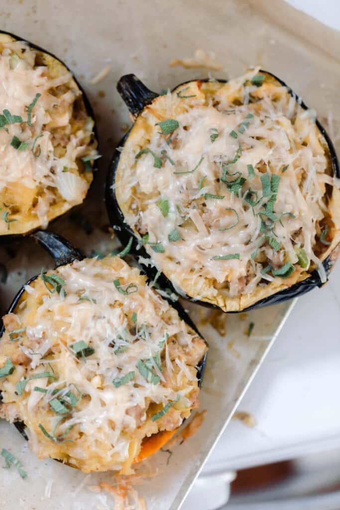 three stuffed acorn squash with sausage, herbs, and cheese on parchment paper