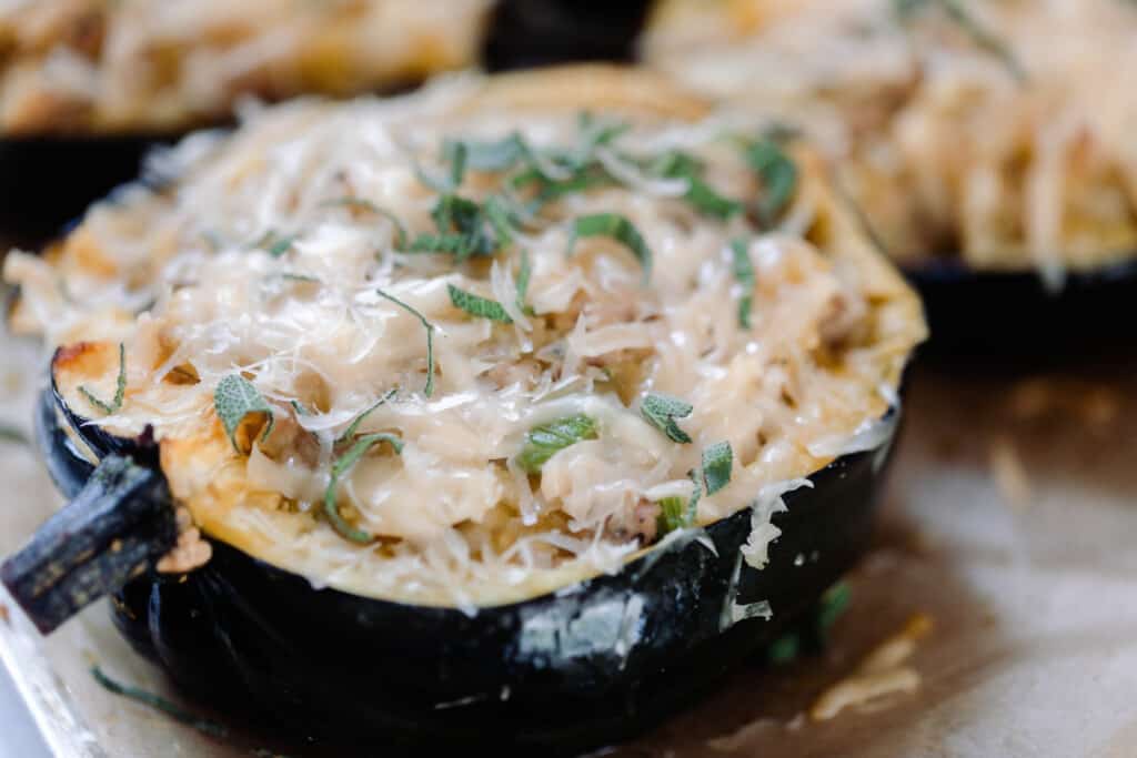 close up picture of acorn squash sliced in half and stuffed with apples, sausage, onions, celery, and topped with cheese and fresh sage.
