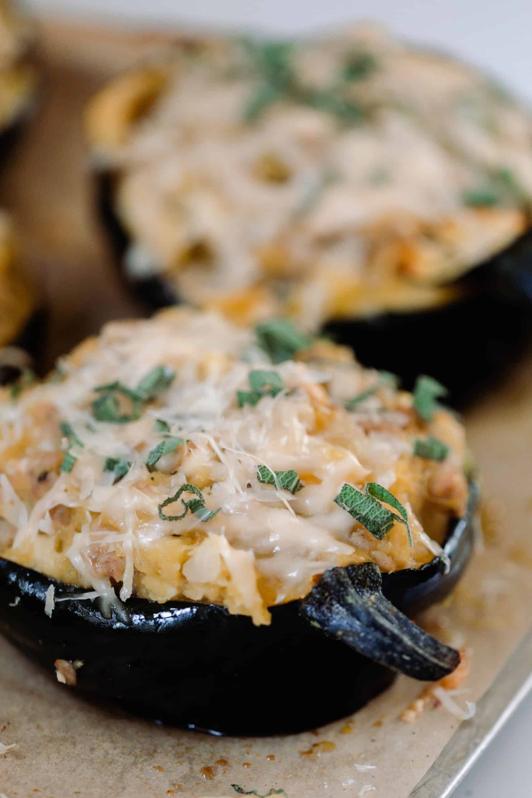 two stuffed acorn squashes topped with cheese on a wood cutting board