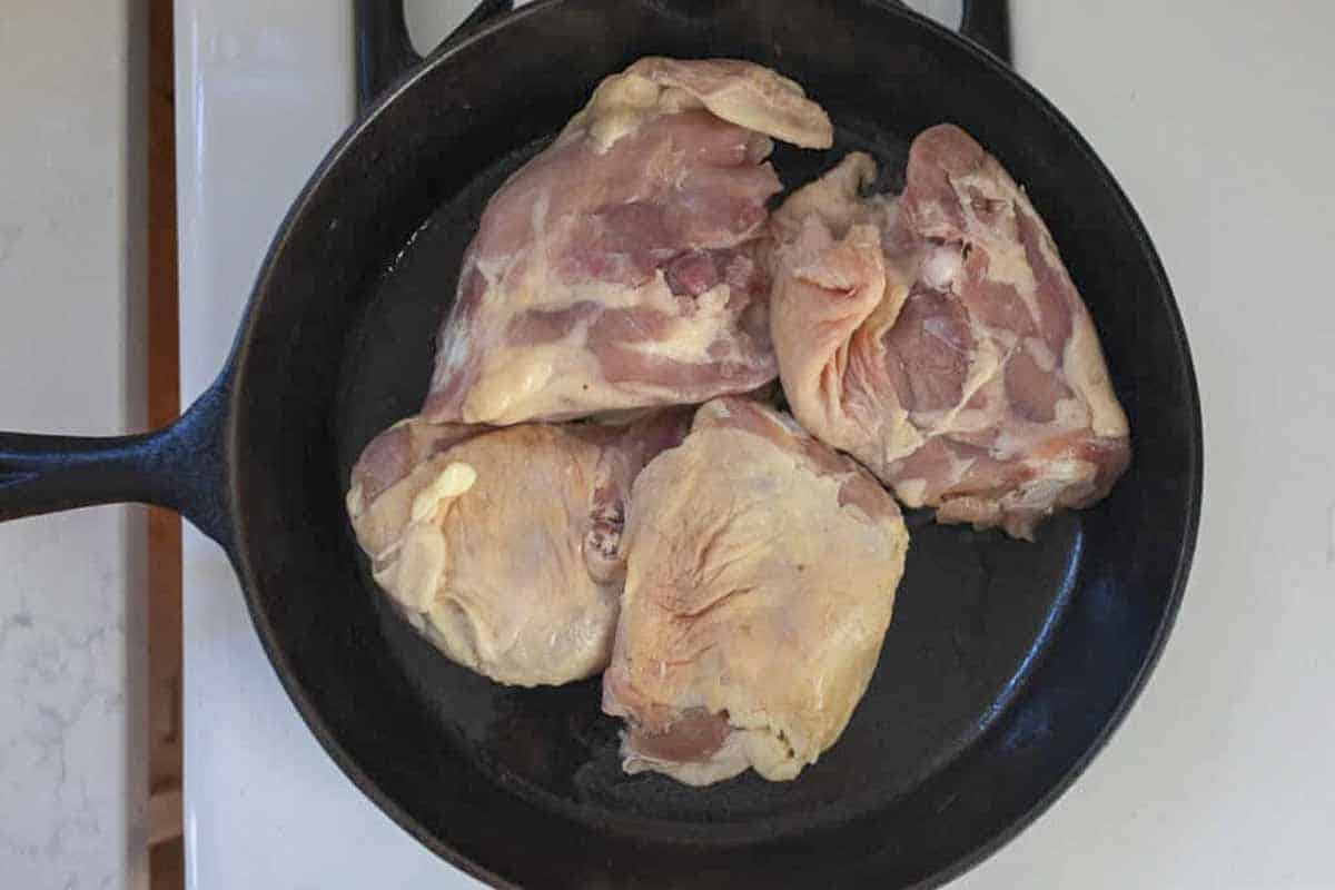Raw chicken thighs in a skillet.