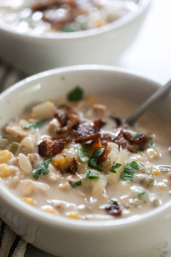 close up picture of a bowl of creamy chicken and corn chowder topped with crispy bacon and parsley