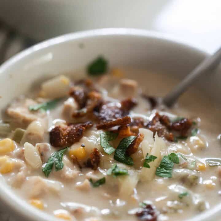 close up picture of a bowl of creamy chicken and corn chowder topped with crispy bacon and parsley