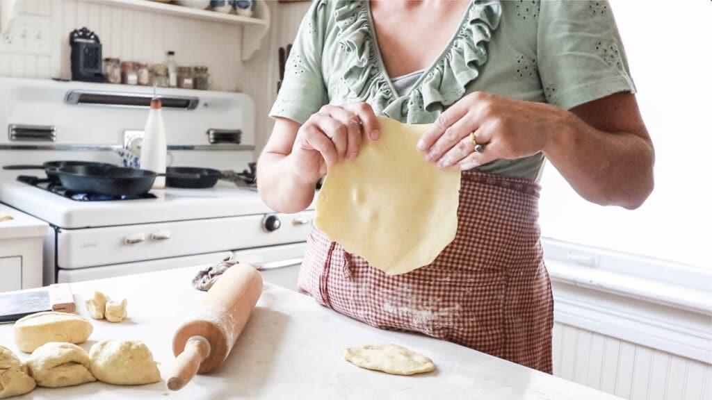 women wearing a green shirt and red apron holding up a fresh tortillas just rolled out