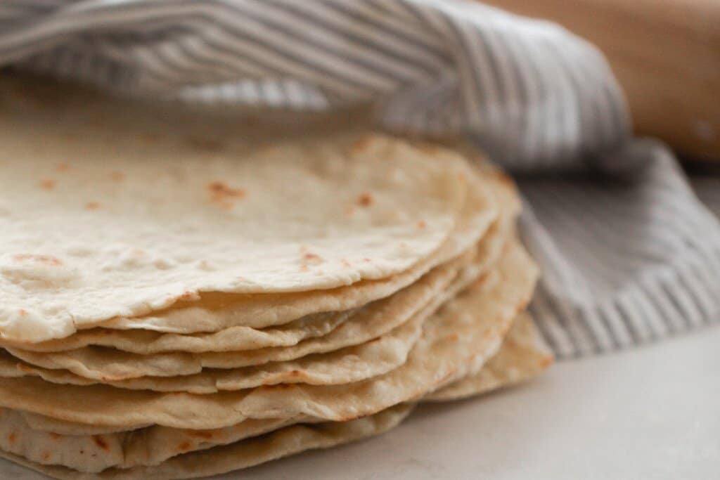 stack of homemade tortillas wrapped in a gray and blue towel
